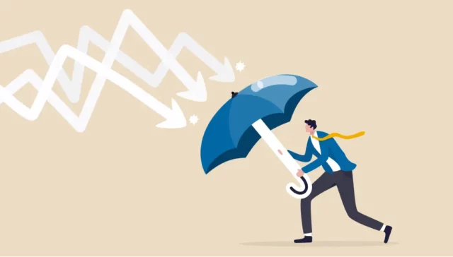The image depicts a person holding a large umbrella, shielding themselves from descending arrows representing declining graphs or data trends. The arrows symbolize a downturn or negative trend, while the umbrella suggests protection and resilience against these adverse conditions. The individual, dressed in business attire, seems to be bracing themselves, indicating a proactive stance against challenges. The image conveys themes of crisis management, risk mitigation, resilience in the face of business challenges, and strategies to safeguard against negative impacts.
