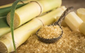 A photo of a spoon full of sugar beside sugar canes for media report on sugar industry issues