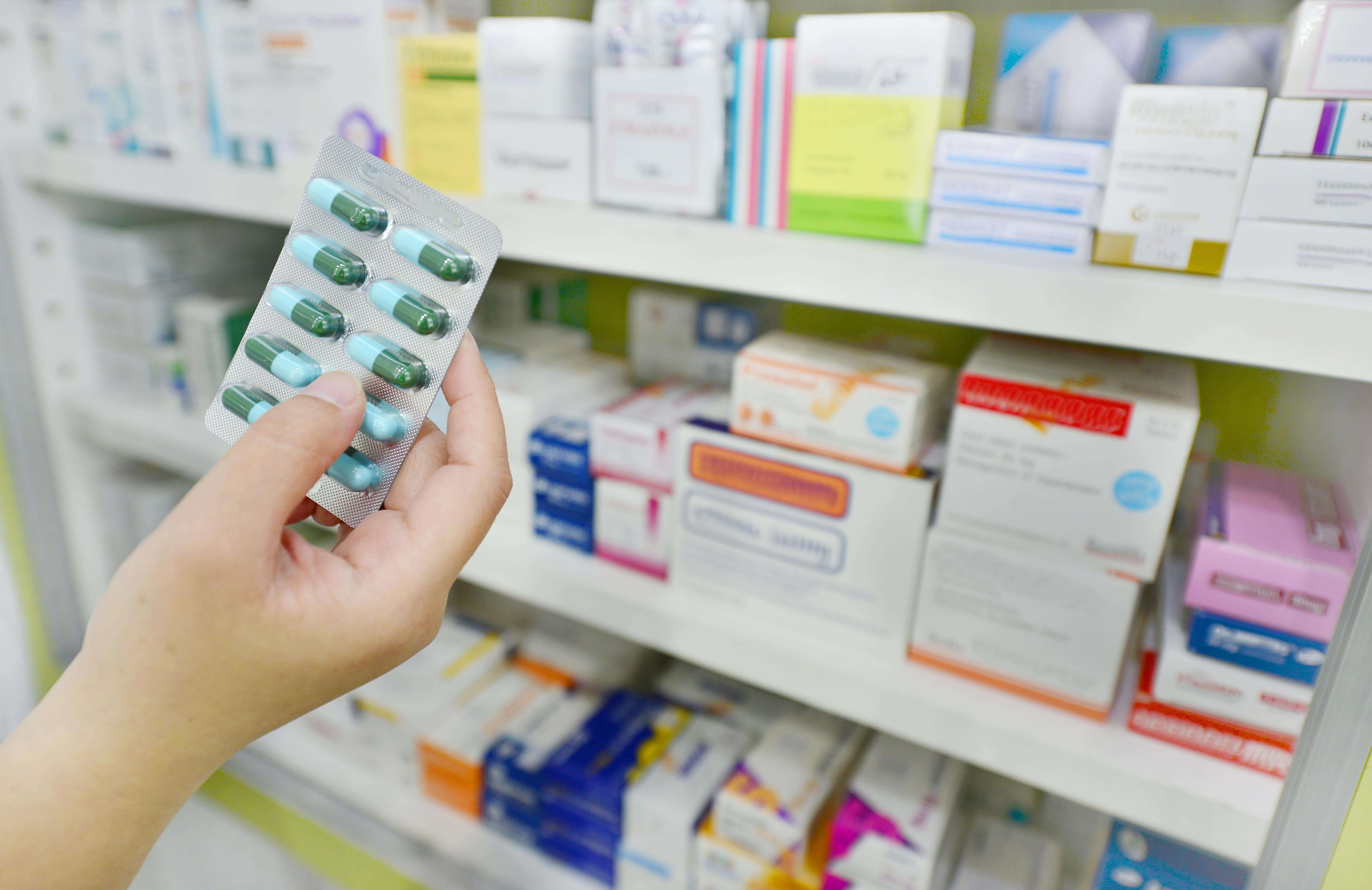 A photo of medicine tablets in the foreground with racks of medicine in the background